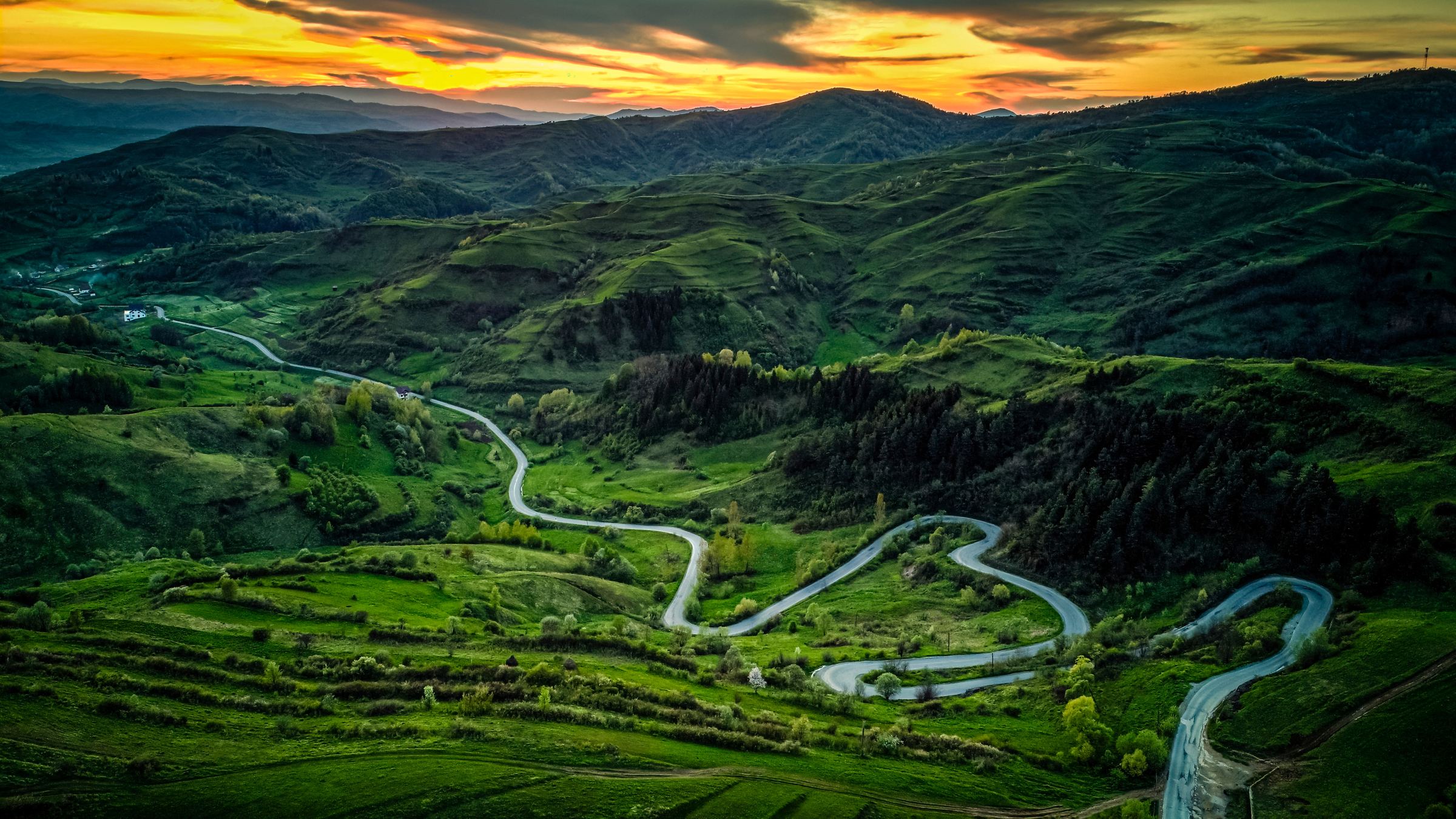 Aerial view of a winding road through green hills at sunset